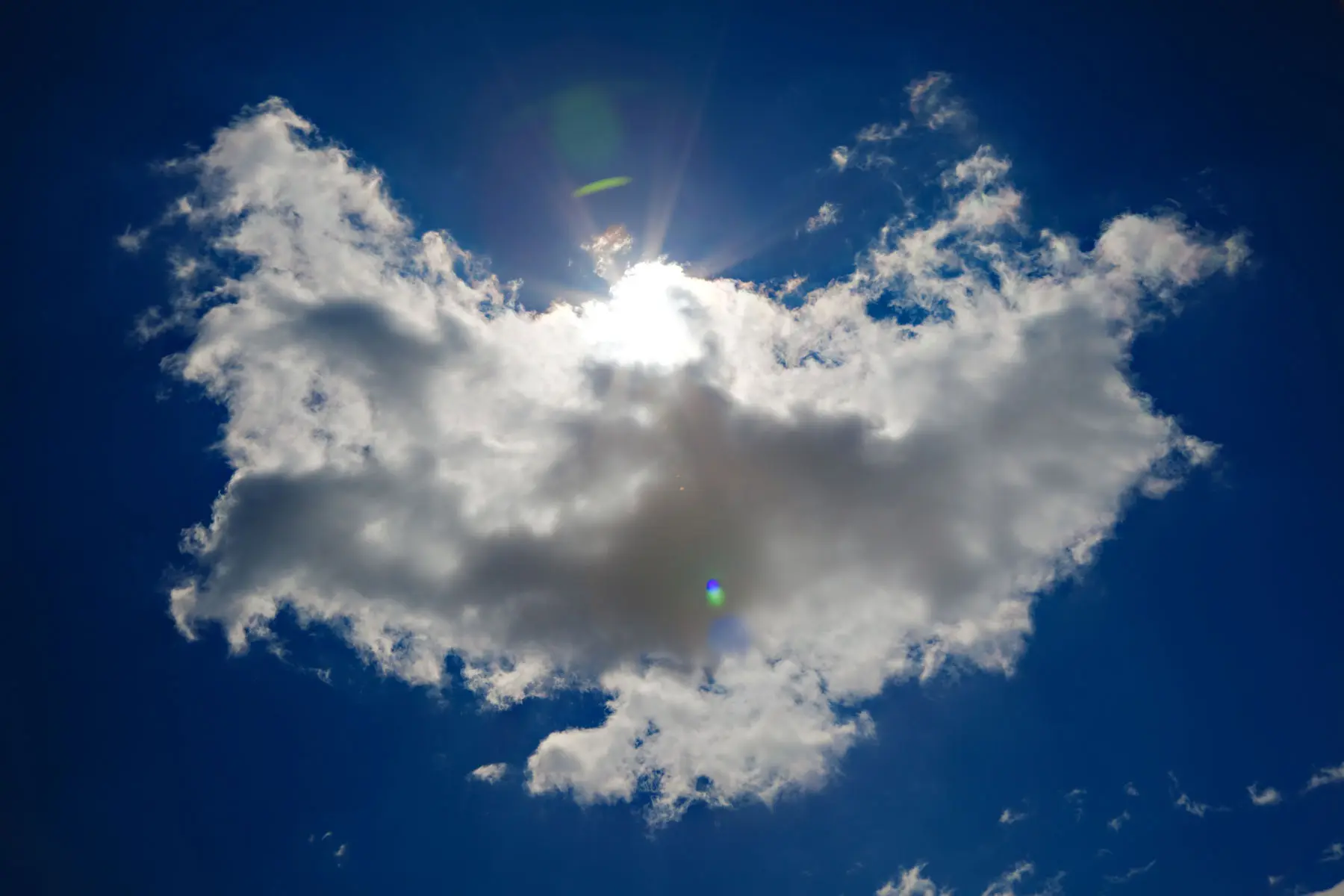 Sunlight breaking through a white cloud shaped like spread wings, high in a deep blue sky.